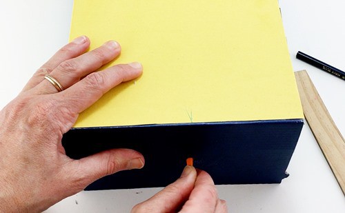 A piece of straw being placed inside a hole centered on a the side panel of a shoebox. 