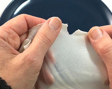  Hands pulling the edge of a sheet of edible paper in opposite directions creating a small tear.  