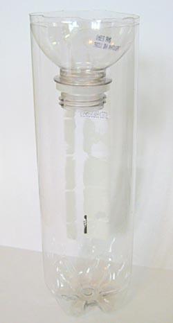 The neck and spout of a plastic bottle is placed upside-down over a cut bottle opening