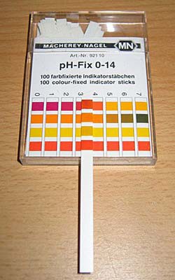 A pH indicator stick lies next to a colored grid to measure the pH of a solution