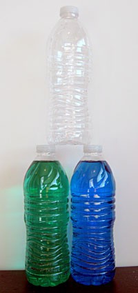 An empty water bottle is stacked on the lids of two full water bottles