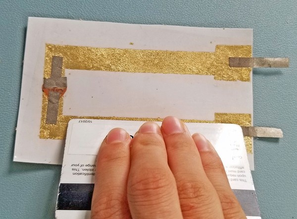 Using a card to press down on adhesive film to better cover circuit 