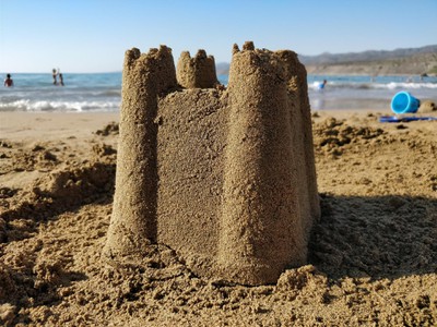 A single sandcastle on a beach, shaped from a bucket with four spires in the corners. 