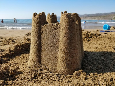 A single sandcastle on a beach, shaped from a bucket with four spires in the corners.