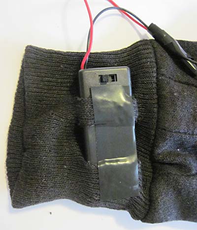 A battery pack is taped to the wrist band of a glove