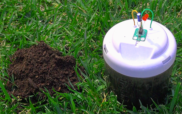 Microbial fuel cell sitting in grass next to a pile of dirt