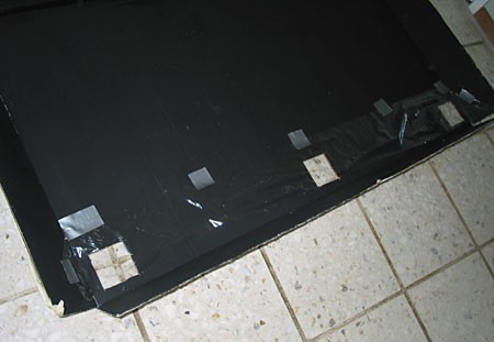 A strip of plastic wrap is taped above three vent holes on the inside of a cardboard sheet and hangs as a flap