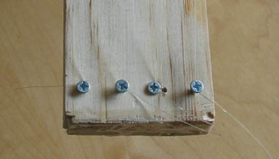 Four evenly spaced screws are placed at the end of a wooden plank in a straight line