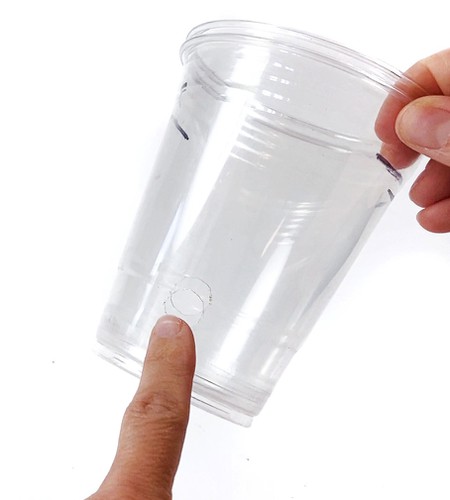 A hand holding two plastic cups. Both cups have a hole in their sides about one inch from the bottom.