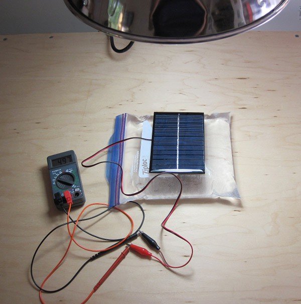 A multimeter connects to a solar cell resting on a bag of water