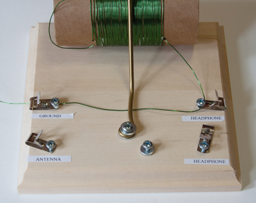 Wire from a homemade crystal radio tuning coil connects to ground and headphone clips