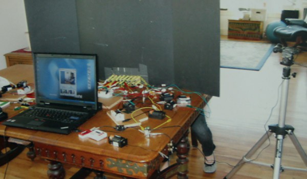 Photo of a computer and video camera on one side of a table and a person hidden behind a divider on the other side