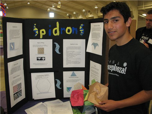 Photo of a student in front of a tri-fold display board decorated with spidrons