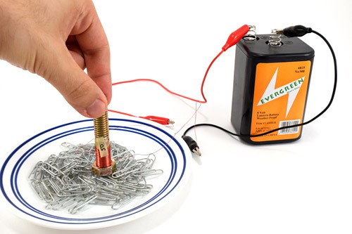A small electromagnet presses against paperclips in a bowl