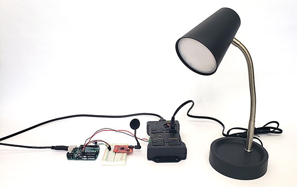 An Arduino next to a breadboard, an electronically controlled surge protector, and a small desk lamp