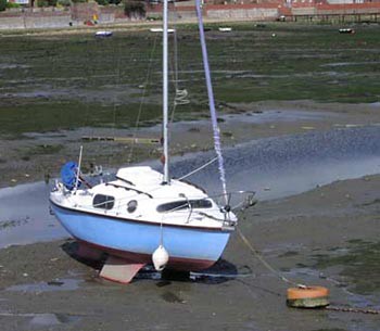 A sailboat with a bilge keel washed ashore on a muddy plain