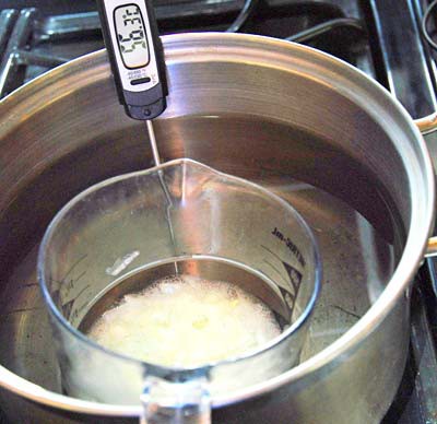 A measuring cup filled with a chopped onion solution floats in a pot of hot water