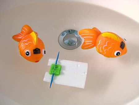 Two toy goldfish and a small white raft float in a pool of water