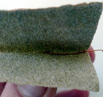 Sandpaper is used to remove insulation from the end of a magnet wire