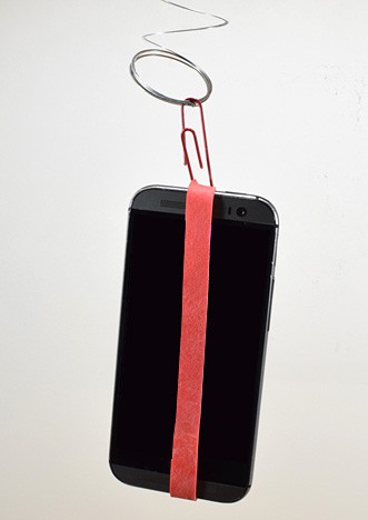 A smartphone is attached to the bottom of a spring with a rubber band and paperclip