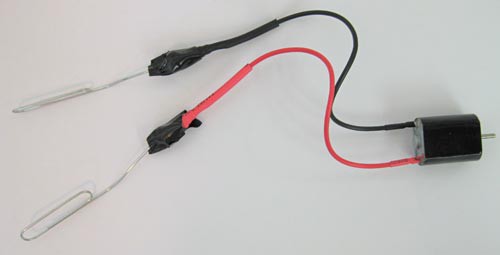 Electrical tape secures two bent paperclips that are inserted into the leads of a small motor