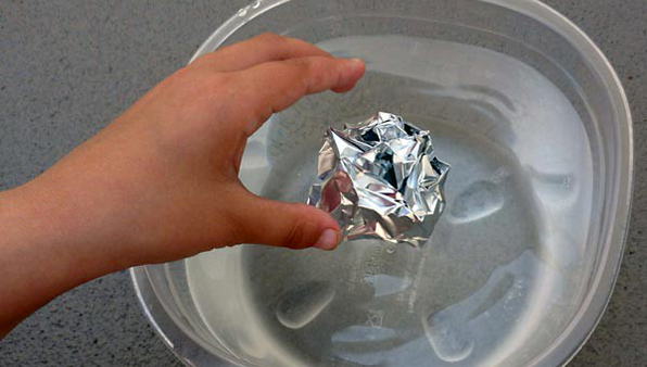 A spherical boat of aluminum foil being dropped in a container of water