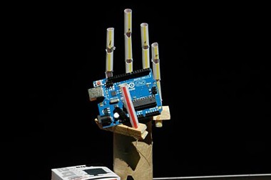 A homemade prosthetic hand holds a microprocessor board next to a servo motor 