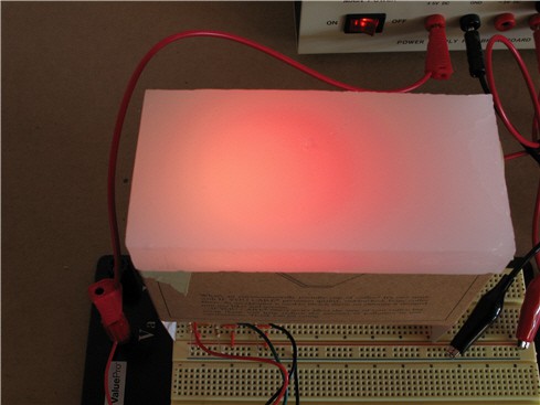 Red light shines through a translucent white block that is placed over the top of a cardboard box