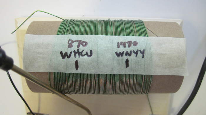 Tape across the tuning coil of a homemade crystal radio is marked with the positions of certain radio broadcast stations