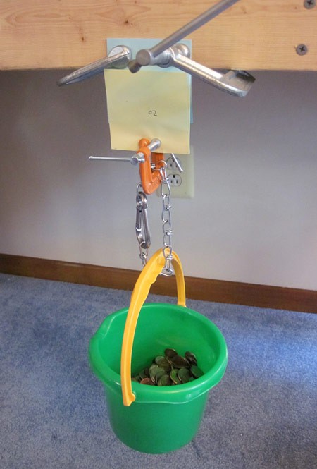 One end of a interlaced paper pad is clamped to a wood frame while a bucket filled with coins is placed on the bottom end
