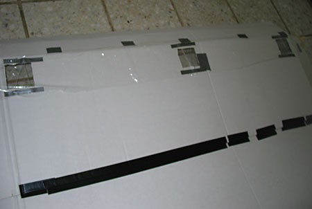 A strip of plastic wrap is taped above three vent holes on the outisde of a cardboard sheet and hangs as a flap