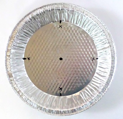 An aluminum pie pan has five black dots marked at the north, east, south, west and center of the pan