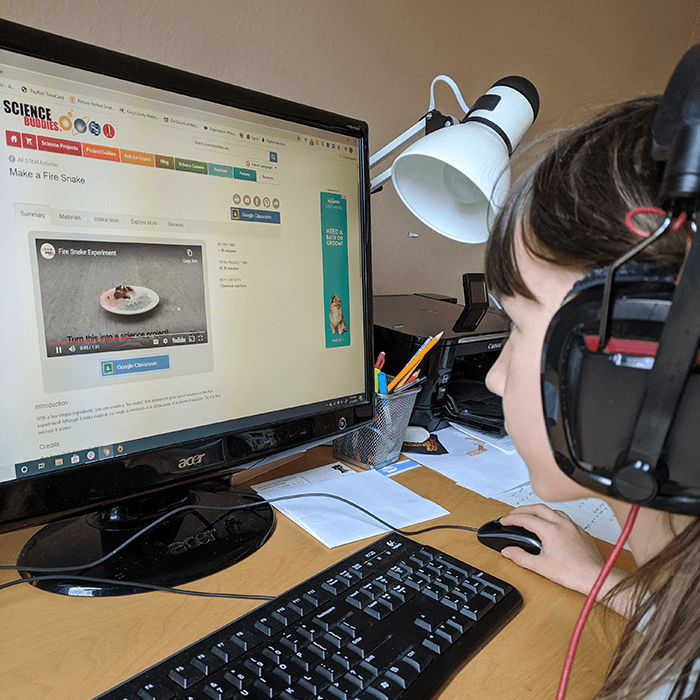 Student wearing headphones and sitting at a computer while watching an online STEM video as part of online learning with her class