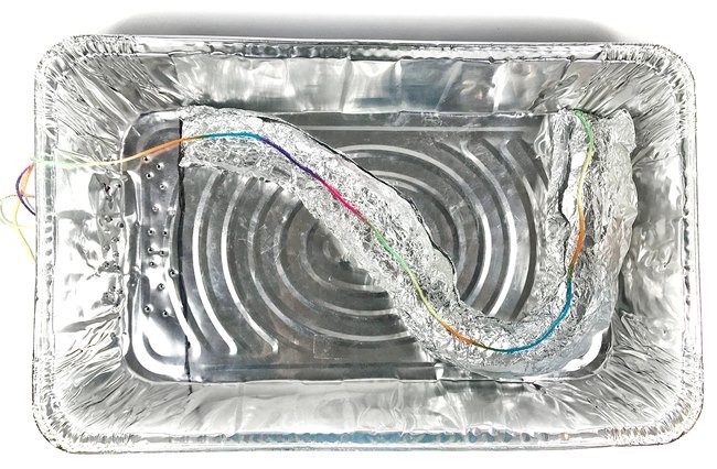 Aluminum pan with a lightly curved aluminum foil river model inside. The length of the river model is measured by laying a string inside the riverbed.
