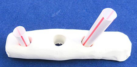 Plastic straws are used to create holes in a piece of polymer clay