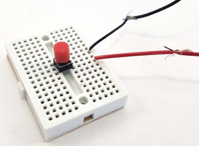 A button on a mini breadboard with two external wires connected 