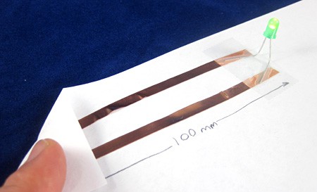 Leads of an LED are taped to strips of copper tape on a piece of paper