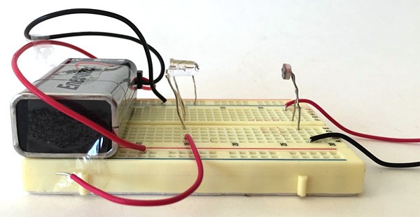 A nine volt battery, LED and photoresistor wired and aligned in a breadboard