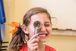 A child holding a magnifying glass up to one eye