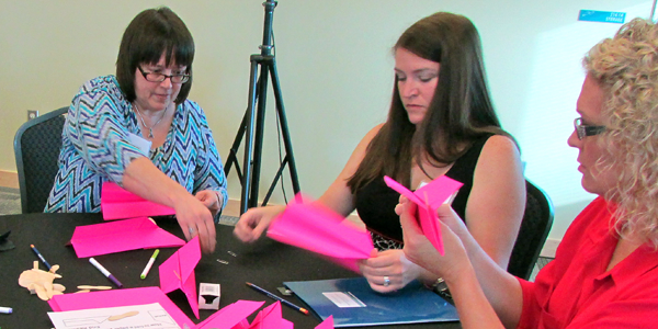 Three woman fold pink paper airplanes