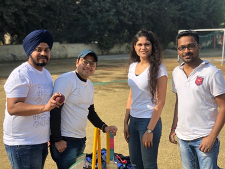Three male and one female engineer dressed casually standing around cricket equipment on a sports field.
