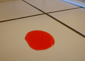 Pool of colored water held together by cohesion and surface tension on kitchen tiles.