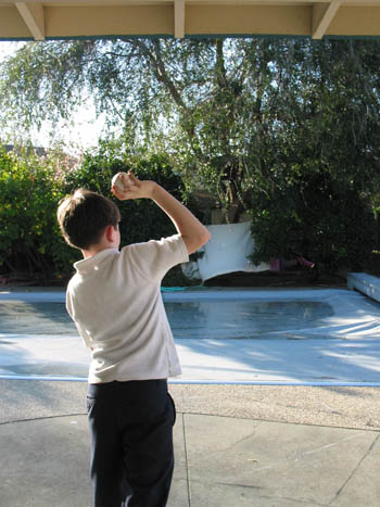 A boy standing upright tries to throw a pitch without taking any steps