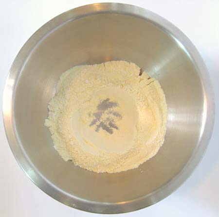 A mixing bowl with the dry ingredients for corn muffins and a hole in the middle.