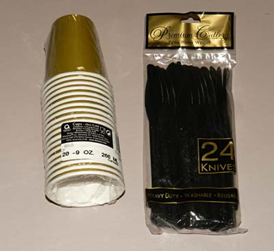 A stack of gold paper cups and a bag of black plastic knifes