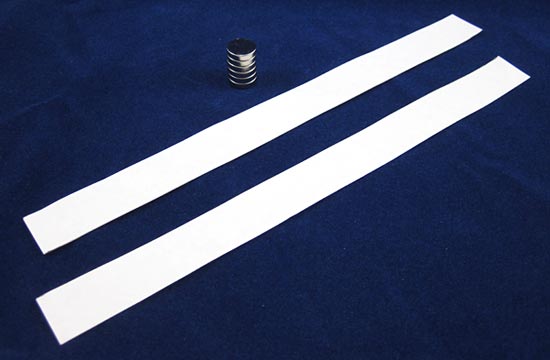Two strips of paper next to a stack of magnets