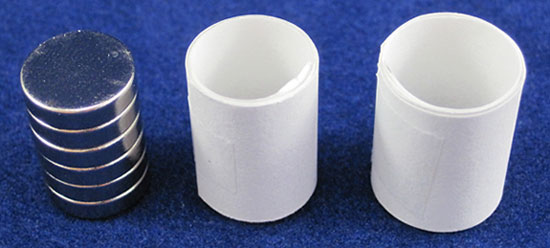 Two paper tubes made of rolled paper strips next to a stack of circular magnets
