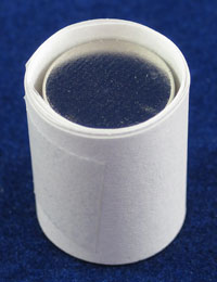 A stack of circular magnets wrapped in a paper strip sit in a slightly large tube made of paper strips