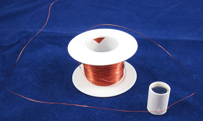 A spool of copper wire next to a stack of circular magnets that are wrapped with a paper strip