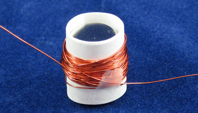 Copper wire wraps around a paper tube that holds a stack of circular magnets